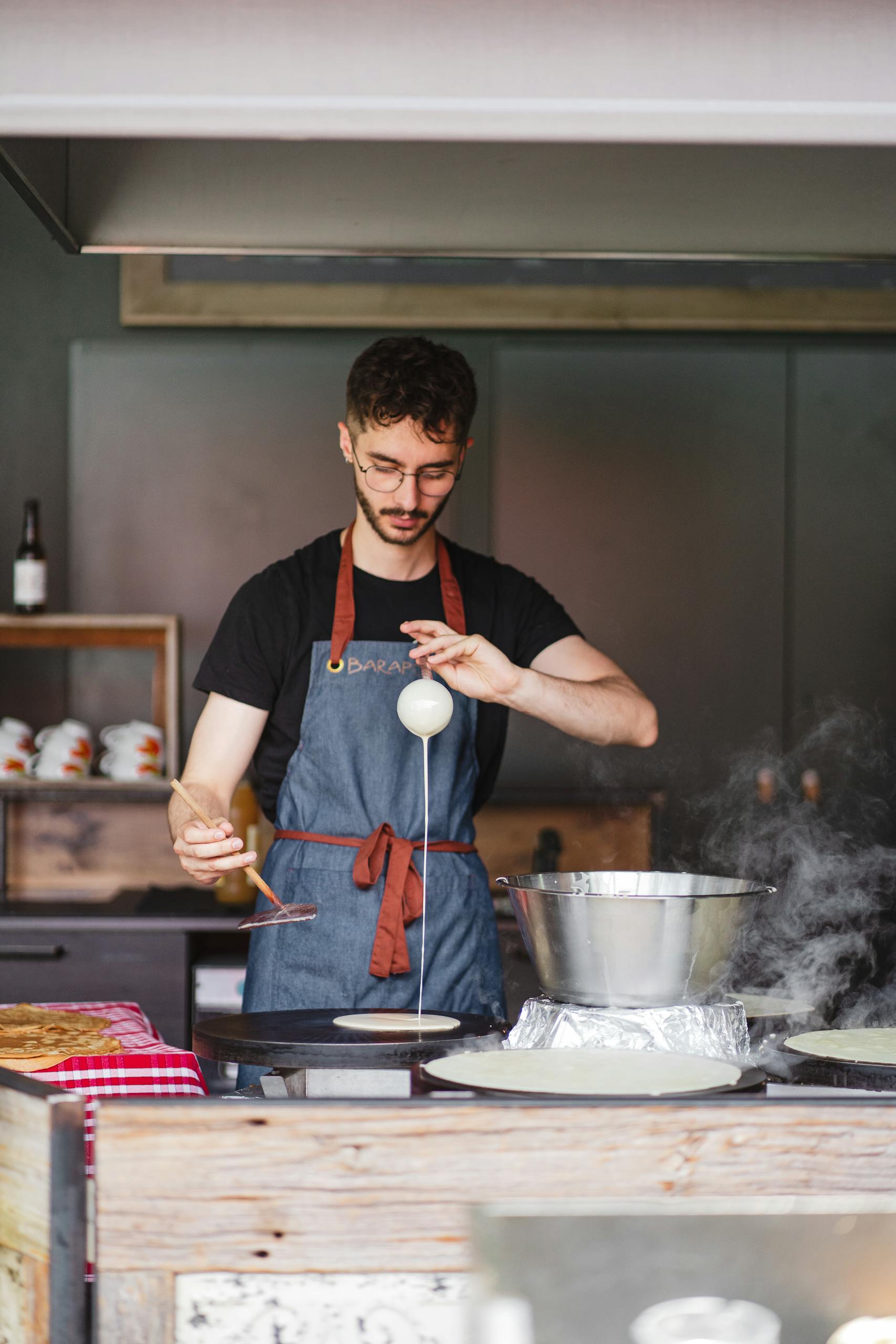 Photo par Clément Proust A chef carefully prepares crêpes in a cozy kitchen setting in Saint-Nazaire, France.